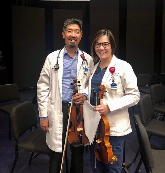 Vincent and Grace Hsu in scrubs and white coats with their instruments.