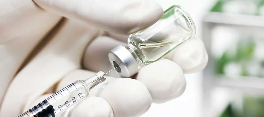 Gloved hand inserting needle into medicine vial