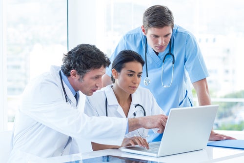 Doctors with stethoscopes huddled together over a laptop in an office to assess data