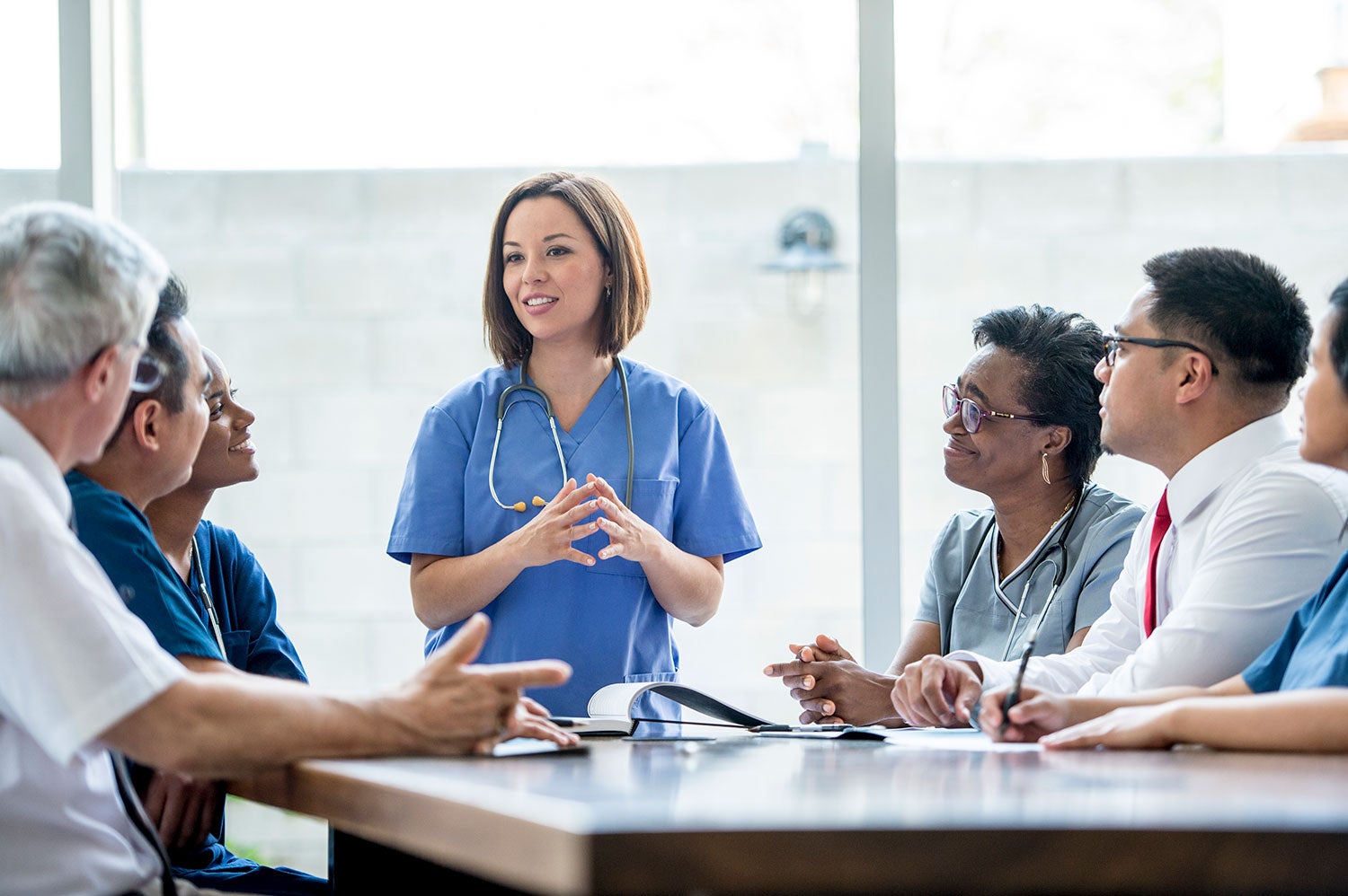 physician stands at head of table smiling and talking with team