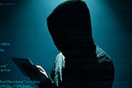 hacker in hooded sweatshirt in a dark room using an electronic tablet