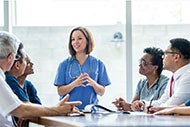 7 Steps to Achieve Organizational Well-Being: Female clinician speaking do other clinicians around a conference table