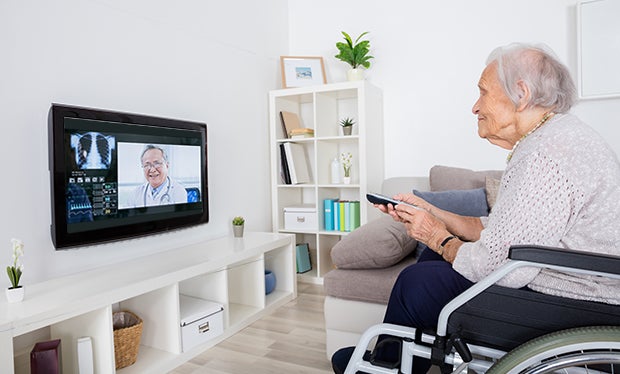 Whoever Controls the Remote May Win with Telehealth. Elderly woman at home in wheelchair speaking with doctor through her television.