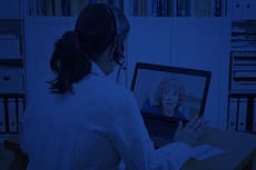 Coronavirus COVID-19 Telehealth and Virtual Care with dark blue overlay. A clinician with a headset on talks through her on a laptop computer to a remote patient at home via telehealth.