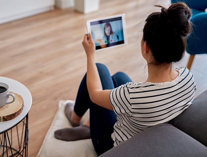 Behavioral Health. A woman in a home holding a tablet which she is using to speak with a doctor through a telehealth app.