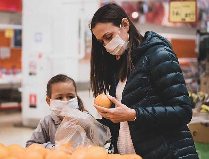 Mother and daughter picking oranges in a grocery store each with masks on