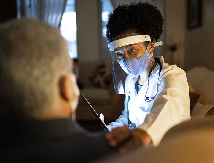 Medical person with face shield and mask on talking to patient