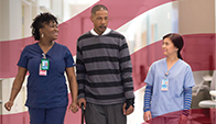 two health workers walk with patient down hospital hallway