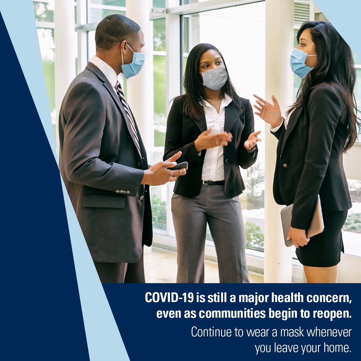 Masked office workers, two female and one male, stand together talking. Caption: COVID-19 is still a major health convern, even as communitites begin to reopen. Continue to wear a mask whenever you leaver your home.