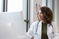 AI in Health Care: Leading through Change. A female doctor works with AI while looking at a computer monitor.
