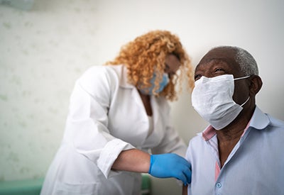 Health worker in scrubs and a surgical mask gives flu shot to woman wearing mask