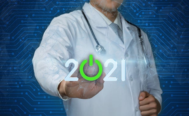 How the Health Care Landscape Will Change in 2021. A clinician wearing a lab coat with a stethoscope around his neck pushing the green "on" button that replaces the zero in 2021.