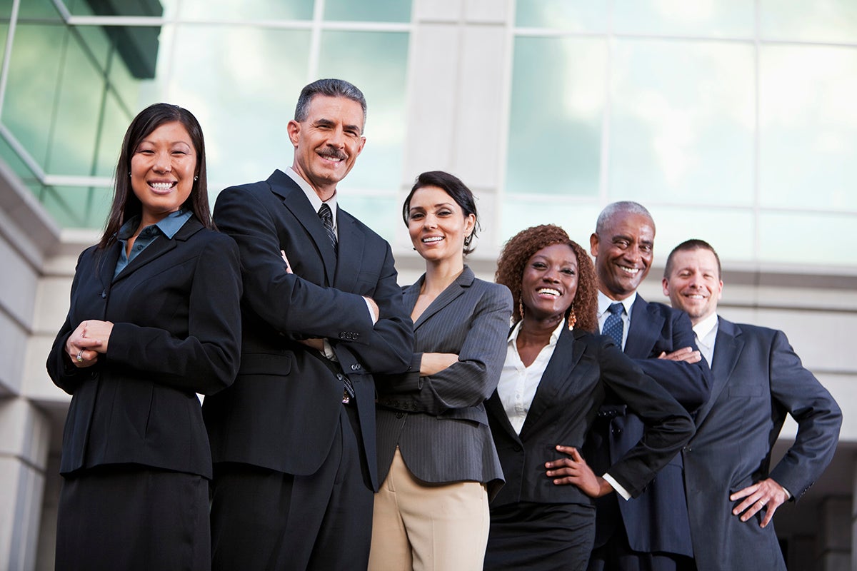 diverse group of business people standing in front of a building smiling