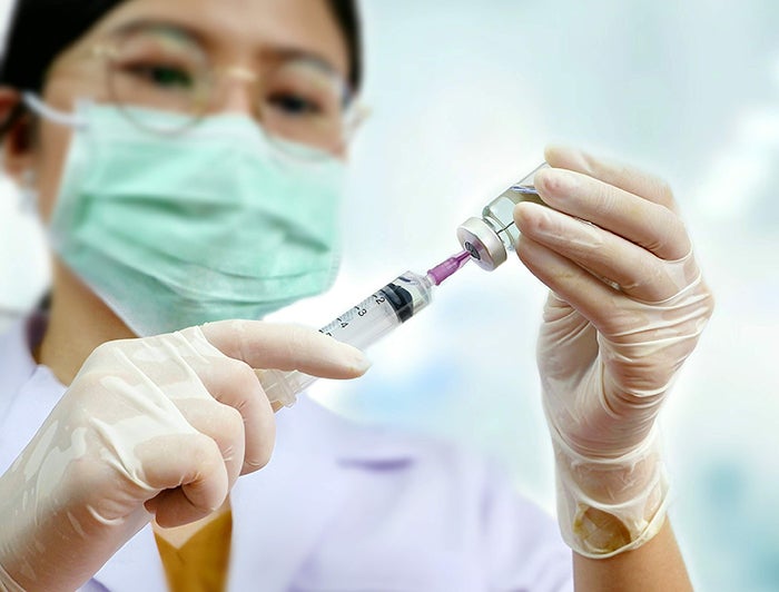 Masked female health worker prepares syringe for vaccination