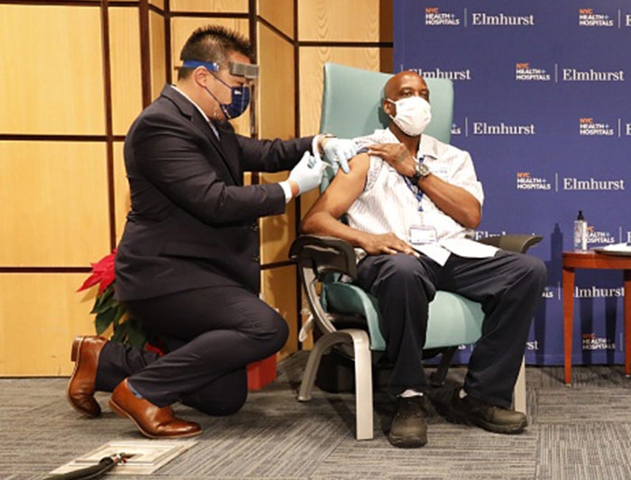 man seated in chair receives vaccine from health worker kneeling next to him