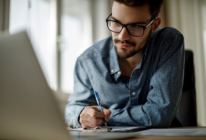 young man taking notes at a computer