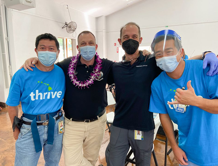 Four men wearing masks stand in a row, arms around shoulders