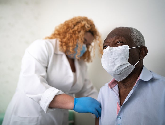 Stock photo of female nurse administering shot to male patient, both wearing medical masks