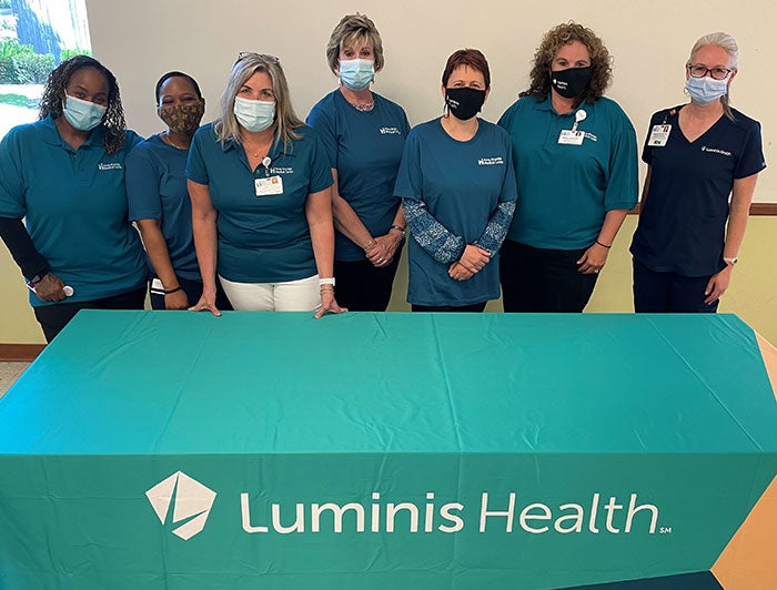 Team of health workers stands in front of a table with the Luminis Health logo