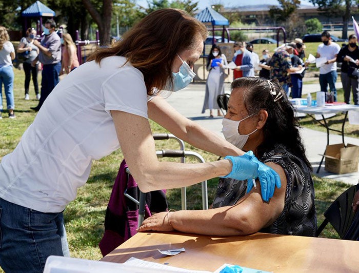 Female patient at outdoor vaccination event is vaccinated by female Sutter health worker