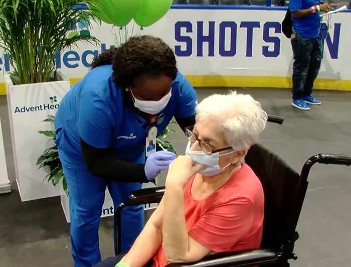 Female AdventHealth worker stands over female patient in wheelchair and administers vaccine