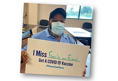Older man holds sign that says 'I miss Family and Friends: Get a COVD-19 vaccine #VaccineHero'