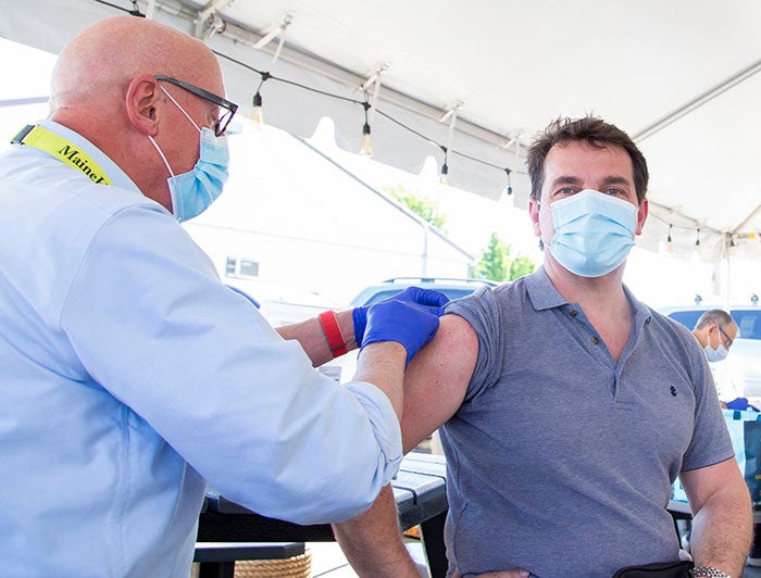 Male Maine Health worker vaccinates a male patient at an outdoor vaccination event