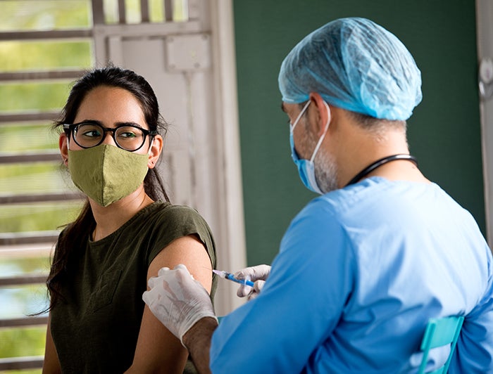 Stock image of a female patient being vaccinated by a male health worker in scrubs and ppe