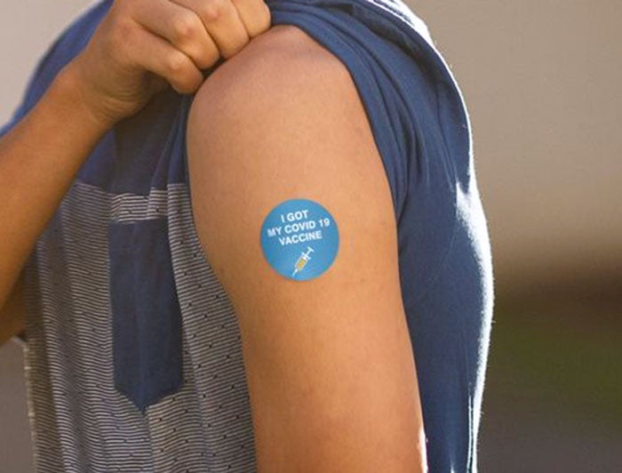 Close up of arm, sleeve pulled up, COVID-19 vaccination sticker on shoulder