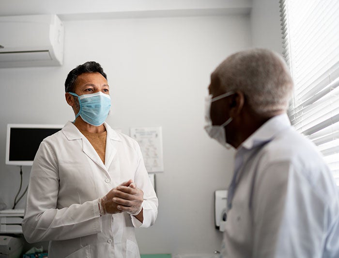 physician and patient wearing medical masks speak in examination room