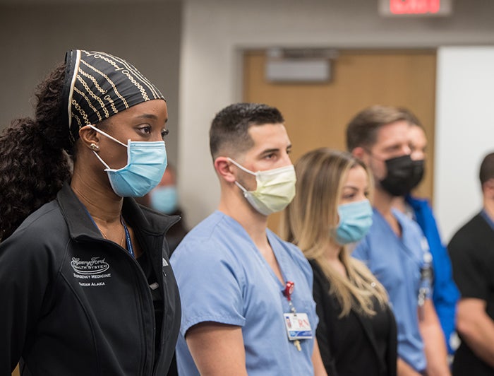 Henry Ford staff wearing PPE standing in a line facing to the right.