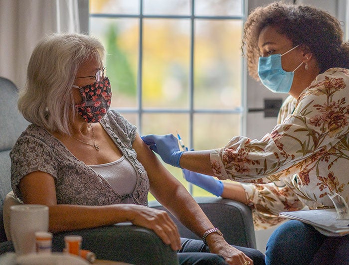 Stock photo of female health worker administering vaccine to elderly patient at home