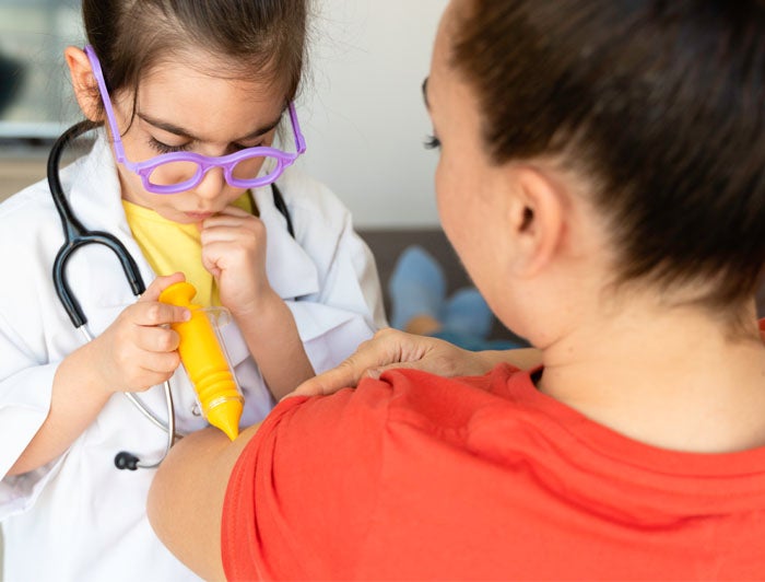 stock photo of young girl playing doctor, using to syringe to give woman shot in arm
