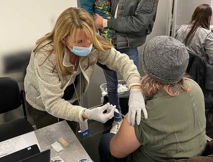 Tufts health worker administers vaccine to seated patient