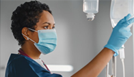 masked health worker inspects IV bag