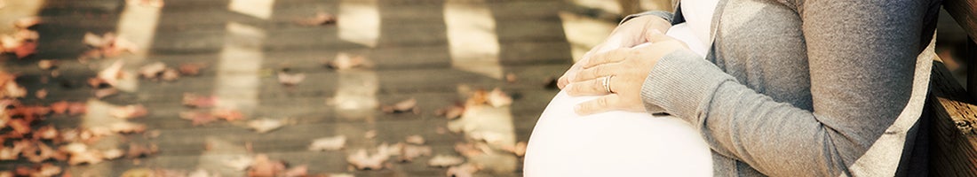 pregnant woman stands with hands crossed on belly on a street lined with fallen leaves