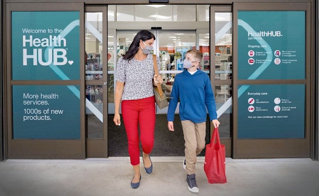 3 Keys to CVS Health’s Growth Strategy. A masked mother and son walk out of a CVS store that has signage on the door that reads Welcome to the Health HUB. More health services. 1000s of new products.