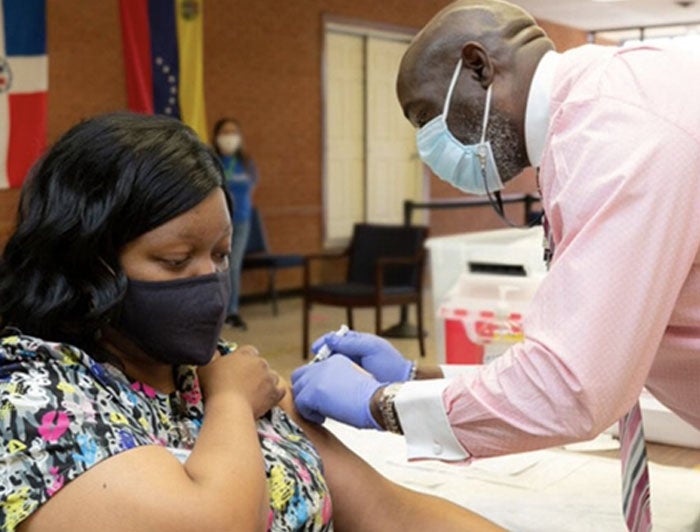 Seated female patient receives vaccine from standing male health worker