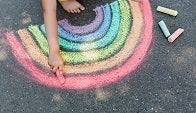A child draws a chalk rainbow on pavement.