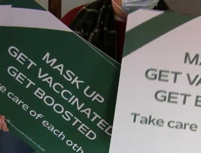 Person holding posters with messages to mask up, get vaccinated, and get boosted