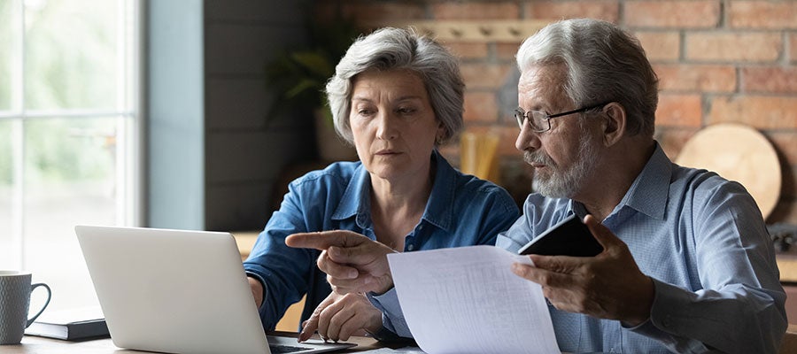 Hospitals and Health Systems Are Working to Implement Price Transparency Policies and Help Patients Understand Costs. An older man and woman review medical billing on a laptop and on a printout. The man is holding a calculator.