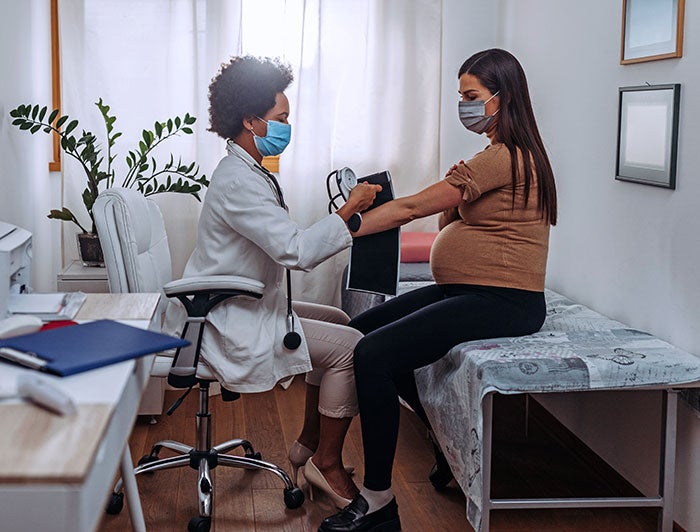 Doctor checking blood pressure of pregnant woman and both of them are wearing masks.