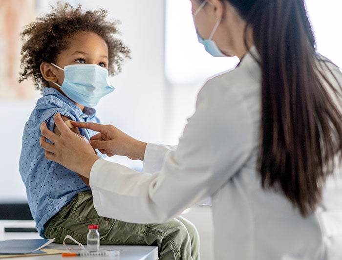 Child being vaccinated against COVID-19 by a medical worker, both of them are wearing face masks