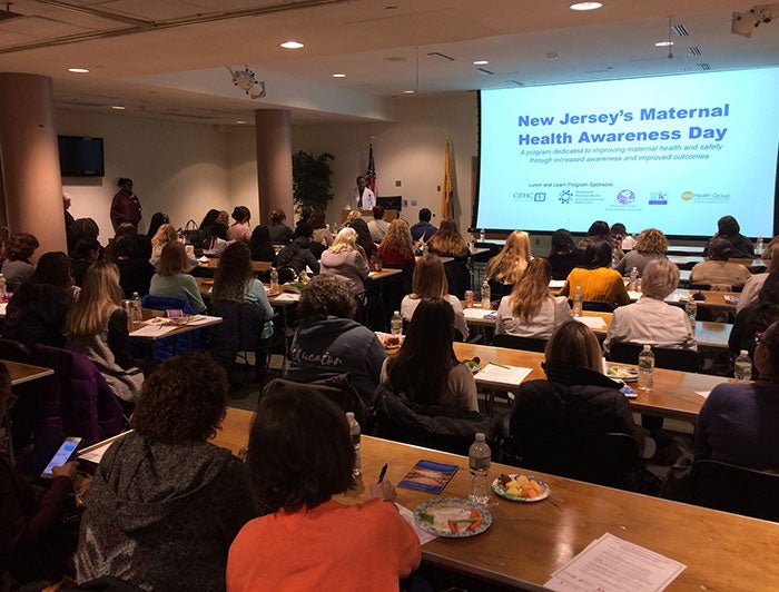 People gathered in a auditorium watching a presentation on New Jersey's Maternal Health Awareness Day