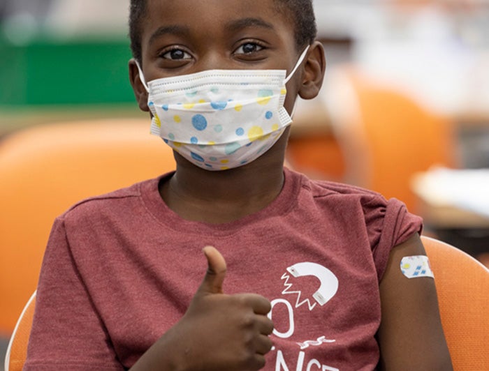 Black boy with bandaid on bicep gives thumbs up gesture