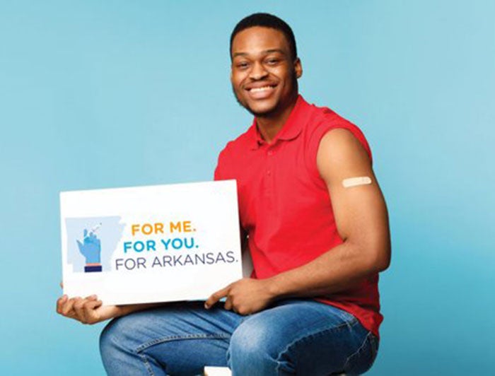 Black man with bandaid on bicep holds sign that says For You. For me. For Arkansas.