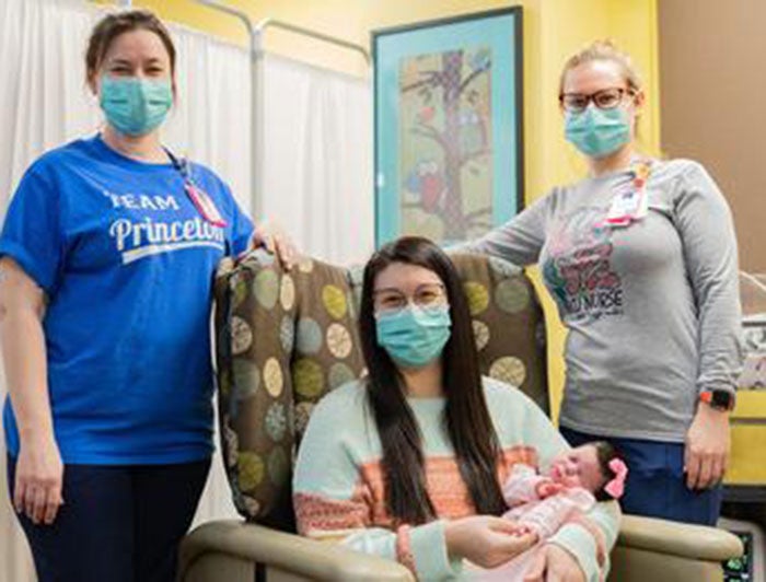 Nurses flank seated patient and baby