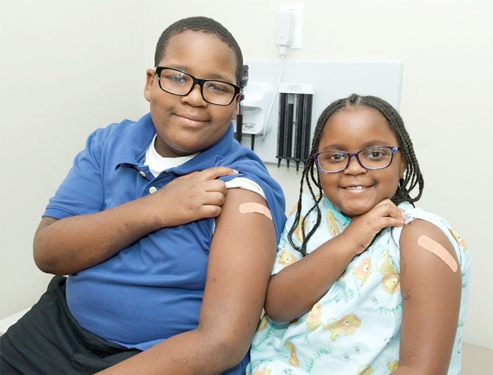 a boy and a girl show off their vaccine bandages
