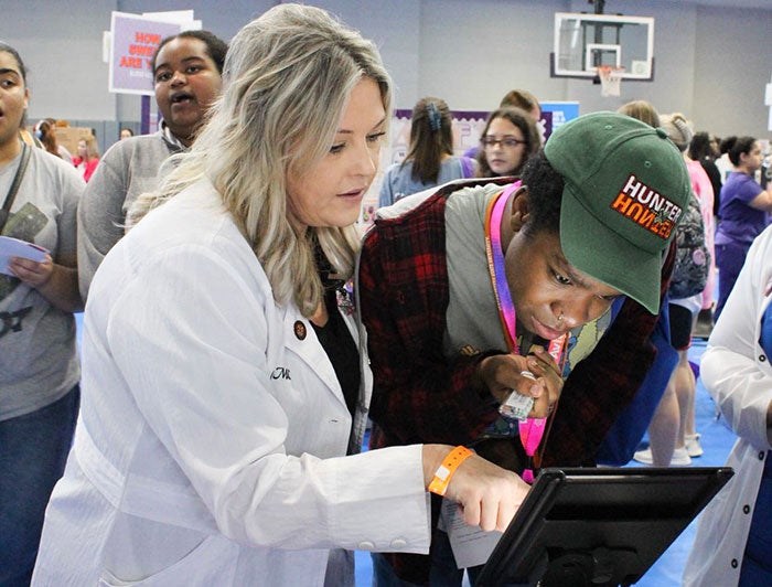 health worker in white coat and community member look closely at a glowing screen