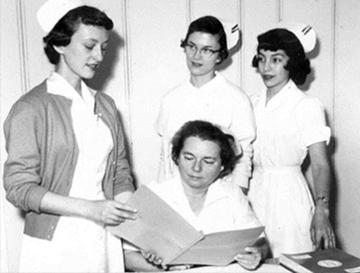 black and white photo of 4 nurses reviewing a chart